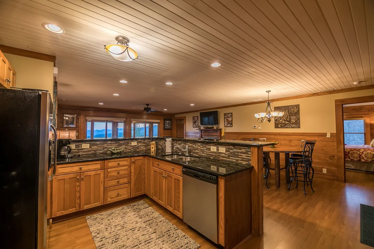 A bright, open kitchen space with a central island, sleek granite counters, stainless steel appliances, and a dining table. Large windows bring in natural light and offer scenic views, making this kitchen ideal for both meal preparation and socializing.