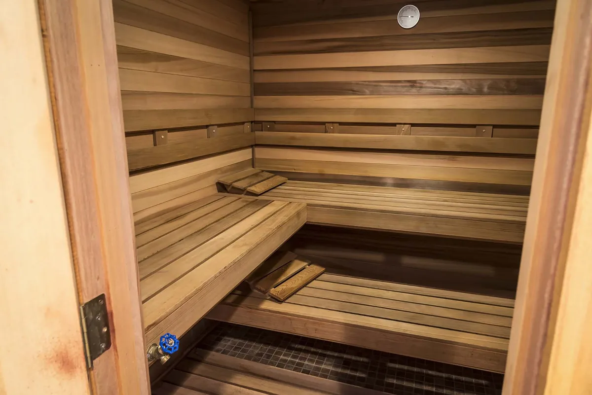 A serene private sauna lined with wooden benches and walls, featuring a classic thermometer. The ambiance is tranquil, designed for relaxation and rejuvenation after a day of activity.