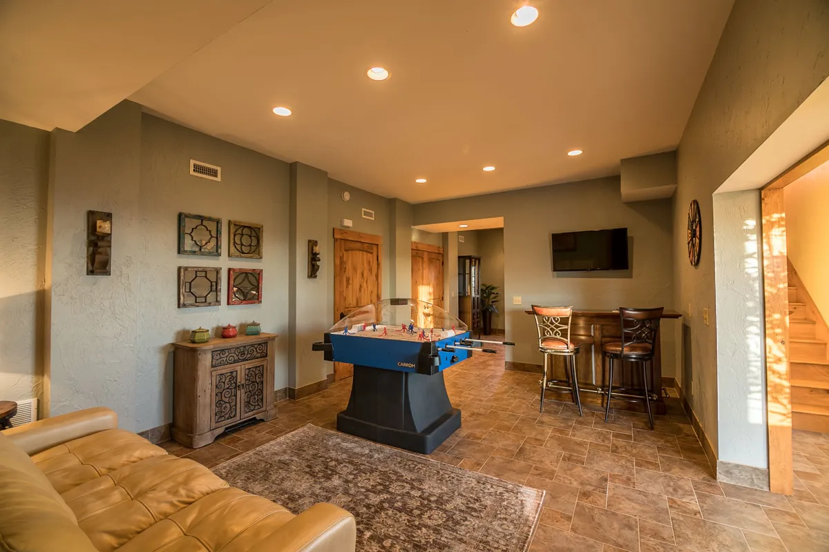 A vibrant game lounge featuring a foosball table, a well-appointed bar area with stools, and comfortable seating. Decorative wall art adds personality, and the space is arranged for socializing, games, and celebratory drinks.