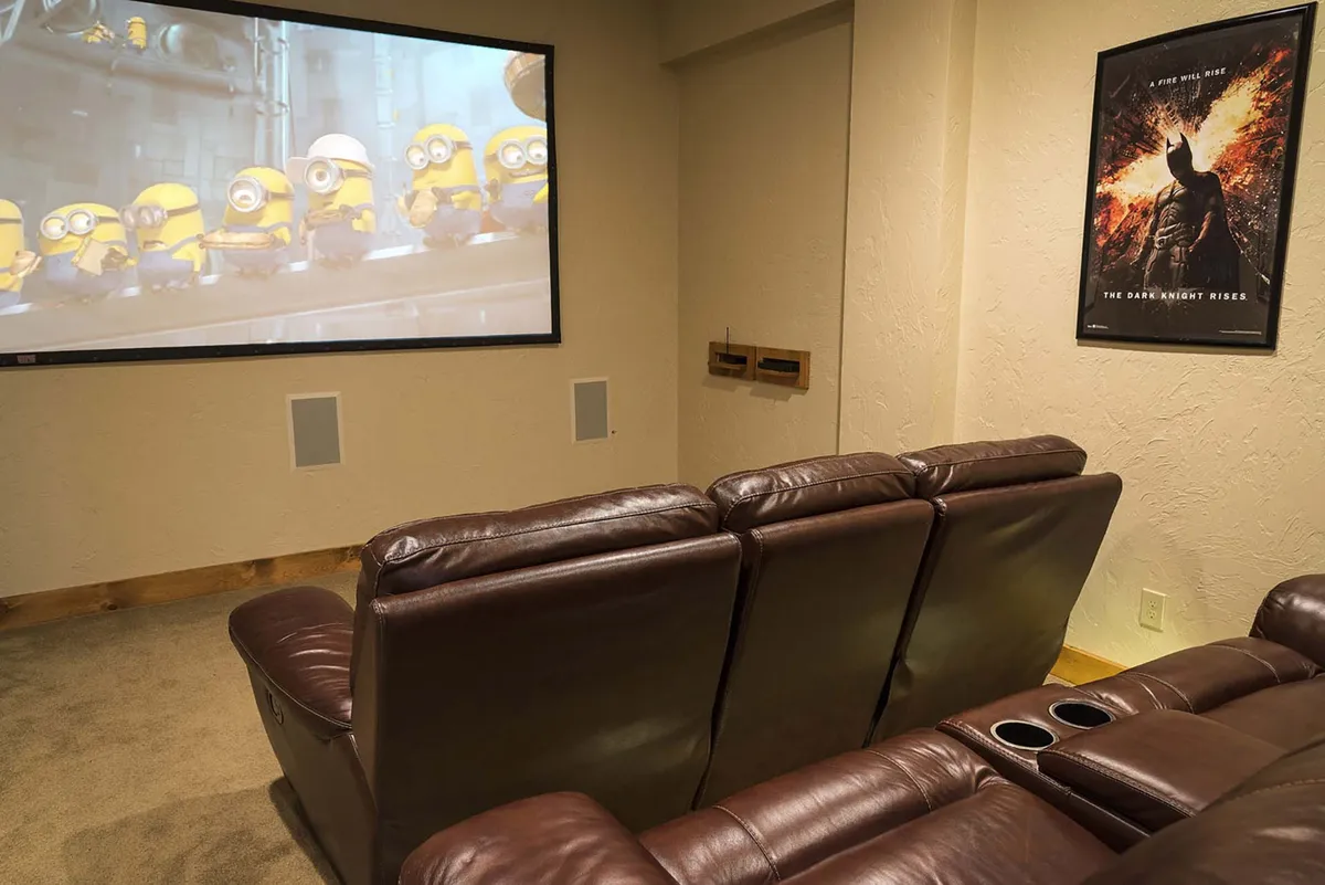 A dedicated home theater space with plush leather seating, a large projection screen displaying animated characters, and a Batman movie poster for ambiance. The room is designed for immersive viewing, with dim lighting and comfortable, tiered seats for a true cinema experience.