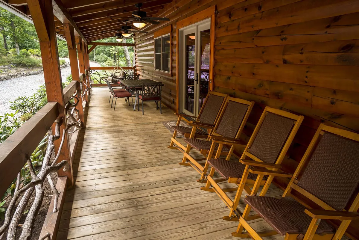 This image features a wooden porch surrounded by natural scenery, with rocking chairs and a table set up for relaxation and conversation. The open design of the porch allows for an immersive indoor-outdoor experience and highlights the connection between the interior space and the surrounding High Country landscape.