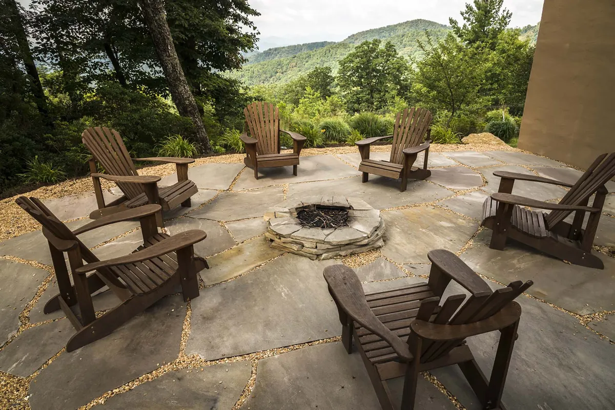 The image shows a stone fire pit encircled by Adirondack chairs, all set against a dramatic mountain view. The setup invites guests to gather around the fire, share stories, and enjoy the outdoors under the open sky, embodying the essence of fireside gatherings.