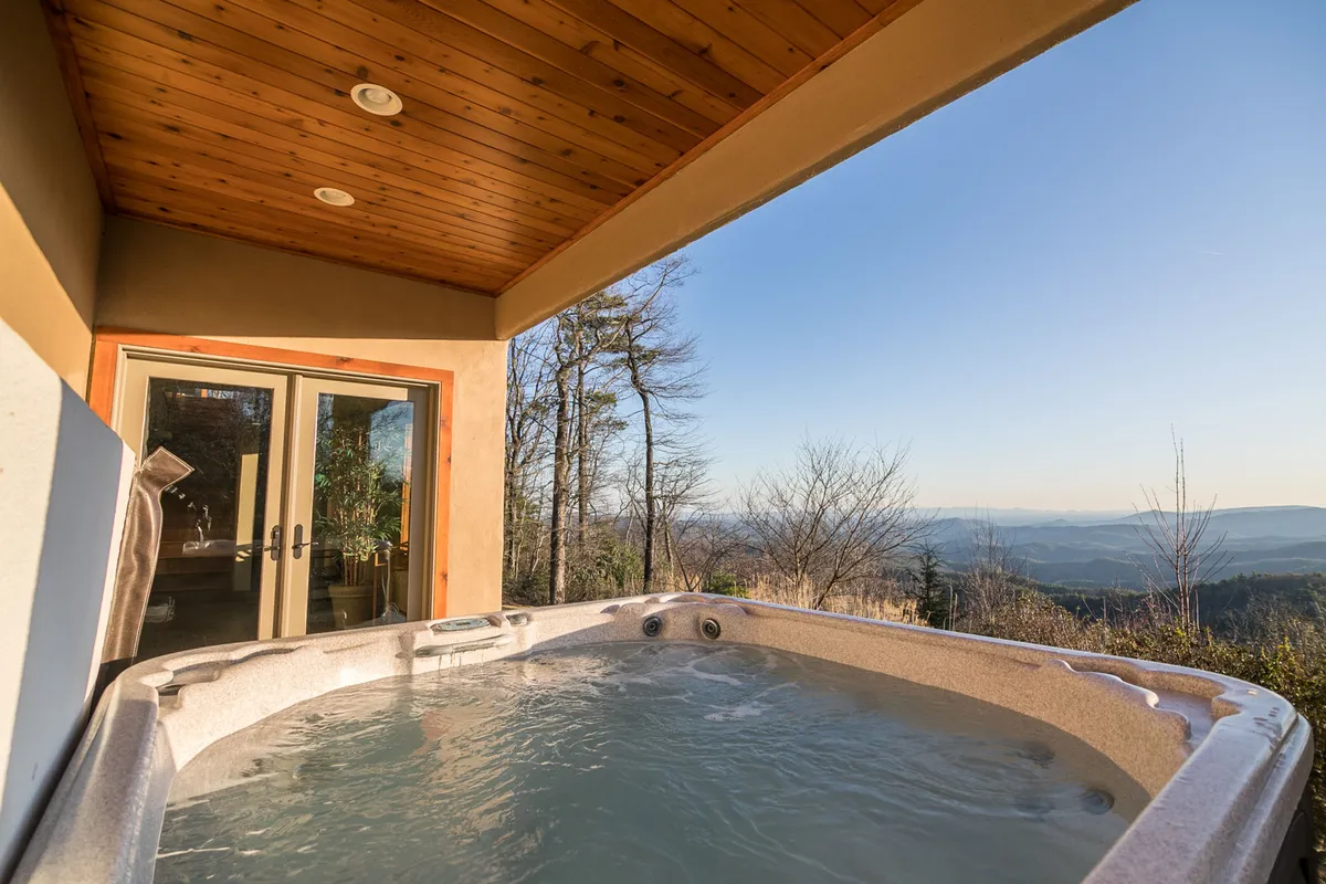 An inviting outdoor hot tub is positioned for unobstructed mountain views, with sleek glass doors nearby suggesting seamless indoor-outdoor living. The tranquil setting is ideal for unwinding in the soothing water while enjoying the landscape.