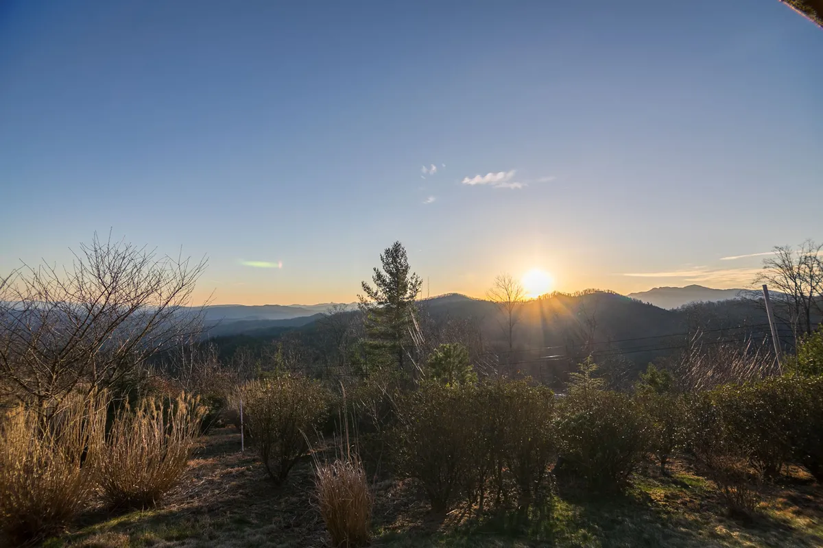 This wide-angle view captures the rolling mountains, trees, and a dramatic sunset sky. The untouched landscape hints at nearby trails and natural beauty, inviting exploration and outdoor discovery.