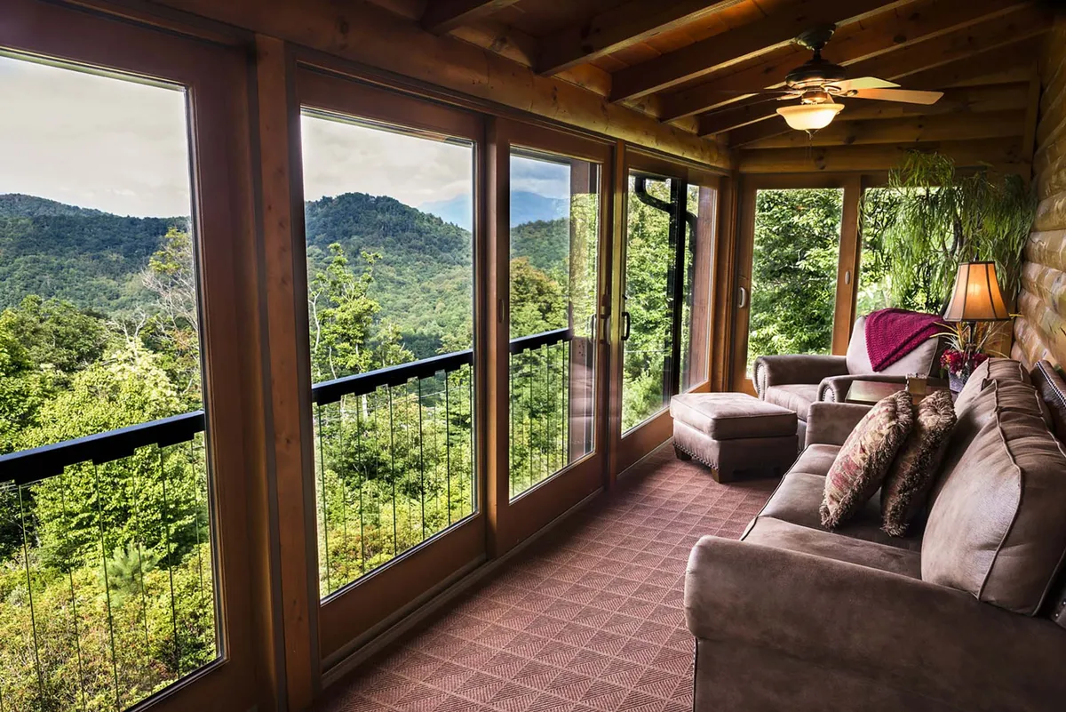 This image features a comfortable sofa and accent chair arranged to take advantage of expansive large windows that showcase a sweeping mountain view. The space is filled with natural light and accented by a potted plant, giving a sense of connection to the outdoors and the tranquil mountain landscape beyond.