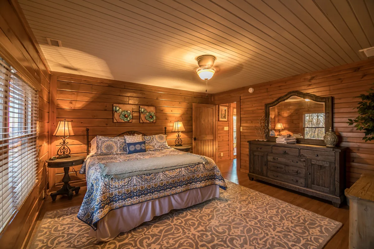 A king suite bedroom with a large bed dressed in patterned bedding, complemented by a wooden dresser and decorative bedside lamps. The room is softly lit, creating a serene atmosphere ideal for relaxation and restful nights.